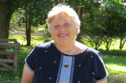 A photo of a lady standing outside in the sunlight with a nice smile