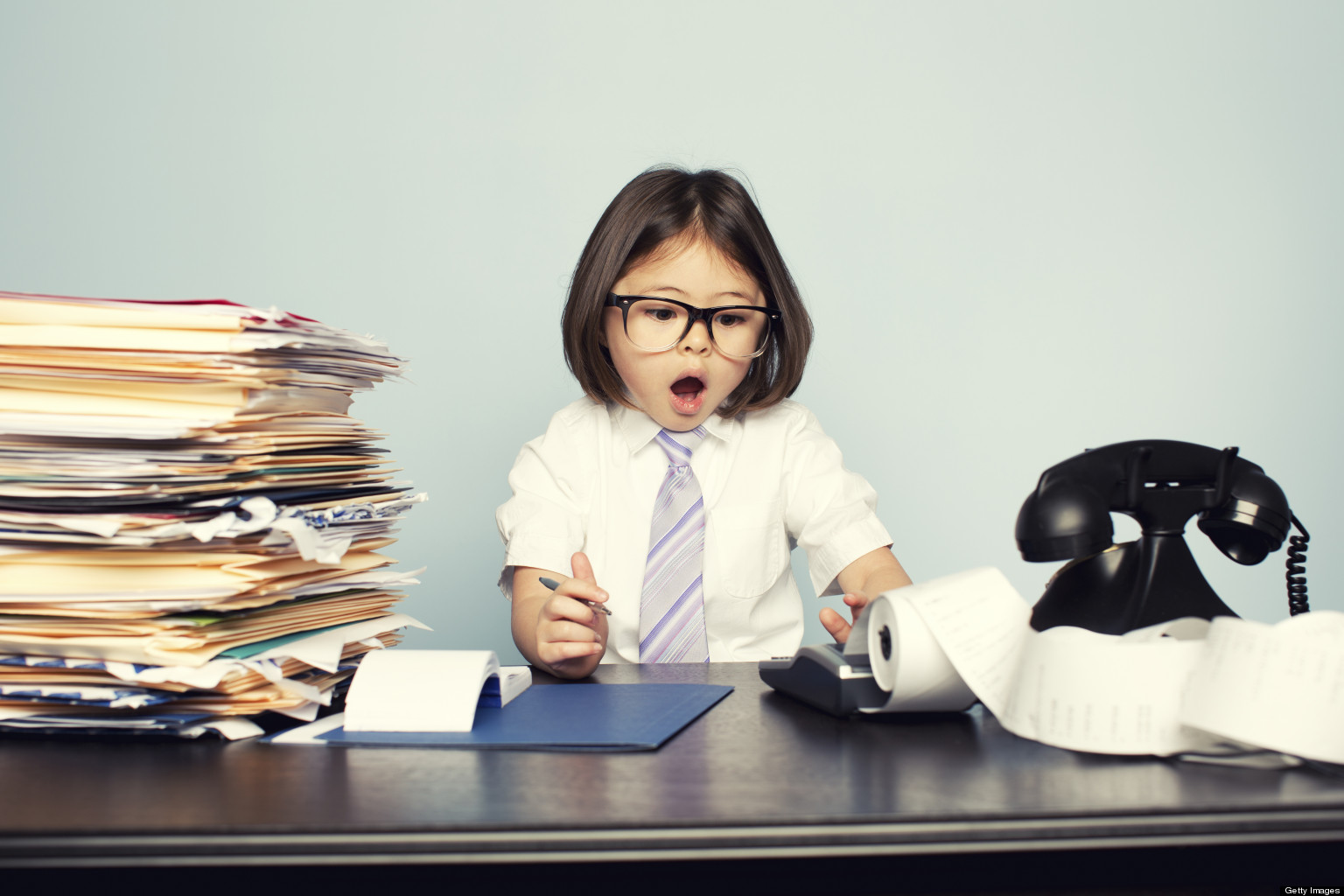 A young kid dressed up as a businessman, looking like he is struggling with his work