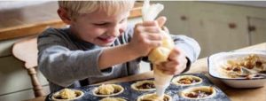A kid, using a piper to fill little pies with icing