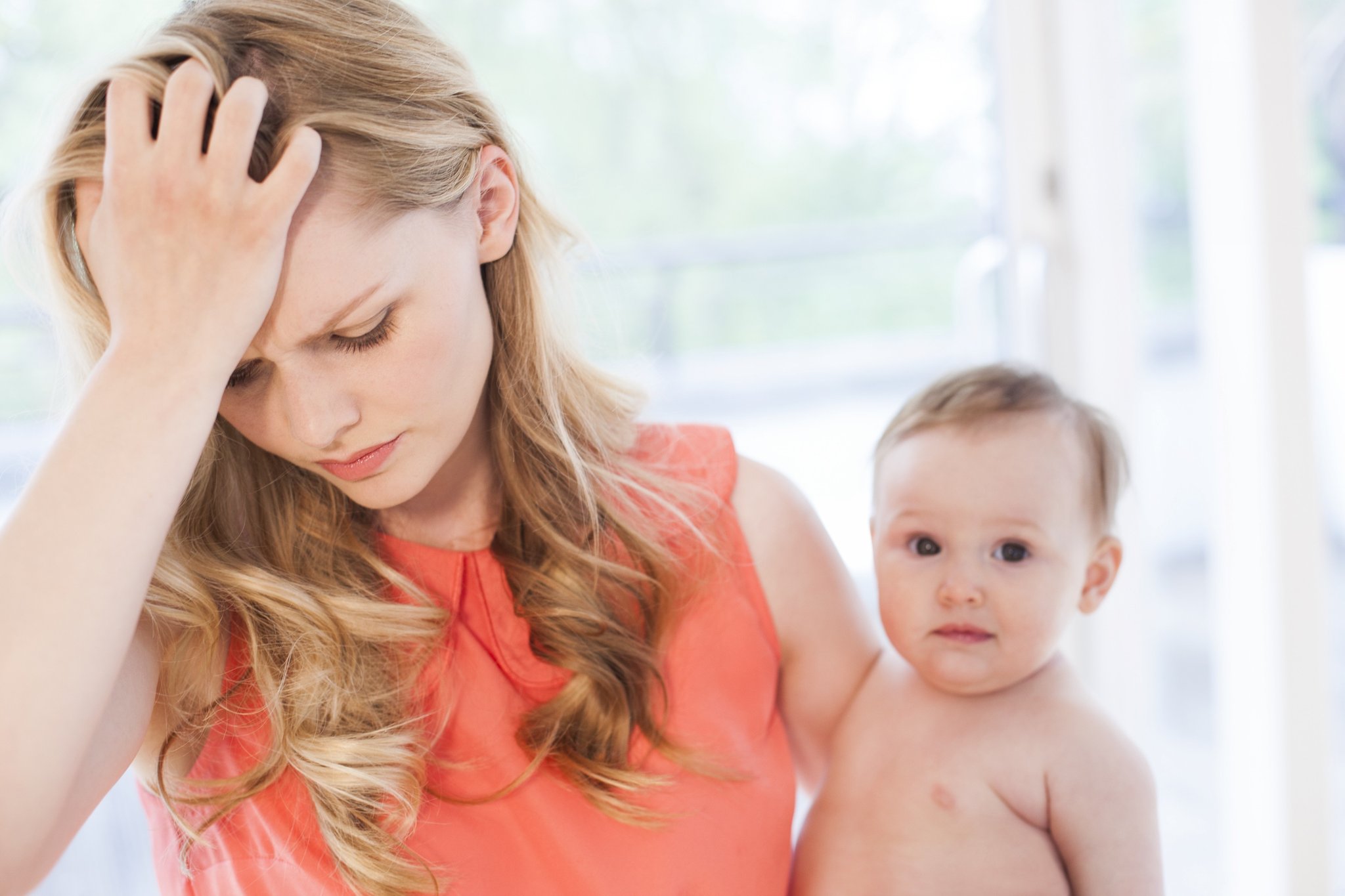 A mom with her hand on her forehead and her baby looking into the camera