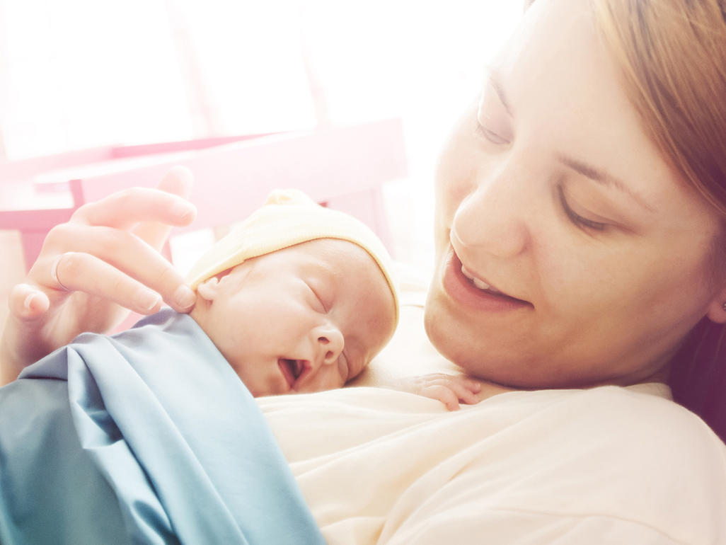 A baby laying on their mothers chest, with the mother looking down at them