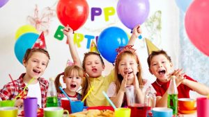 A birthday party for some children, all wearing birthday hats with rainbow balloons