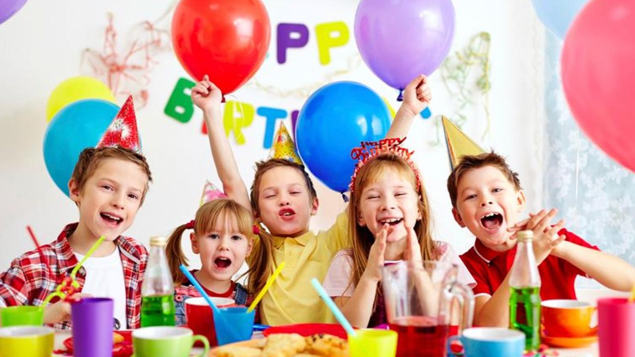 A birthday party for some children, all wearing birthday hats with rainbow balloons