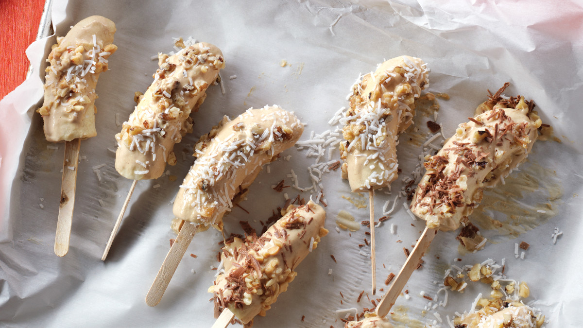 Frozen bananas on a stick covered in nuts and coconut shavings