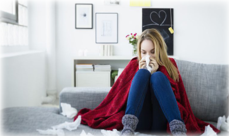 A women under a blanket, surrounded by used tissues blowing her nose