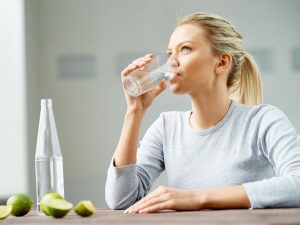 A women drinking a glass of water, with some limes on the table