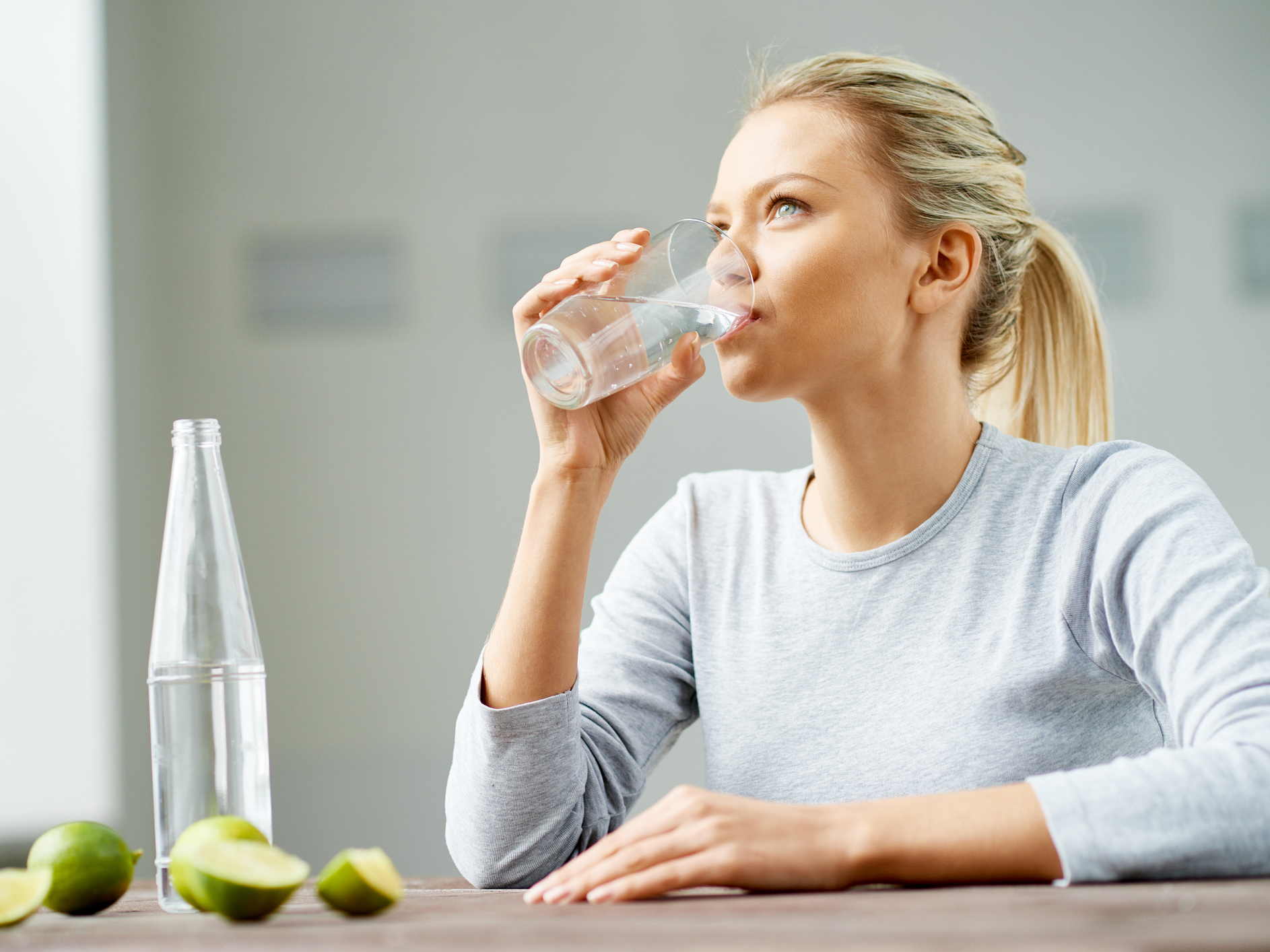 A women drinking a glass of water, with some limes on the table