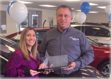 A picture of a man and a women holding an award at a car dealership