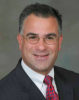 A closeup headshot of a man in a suit and tie