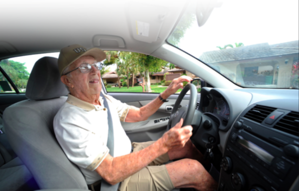An older man driving his car, he's wearing a hat and glasses