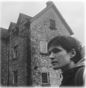 A black and white photo of a man standing next to a cobblestone home