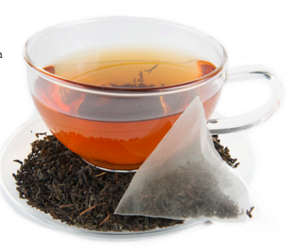 A clear cup filled with tea, surrounded by tea grounds