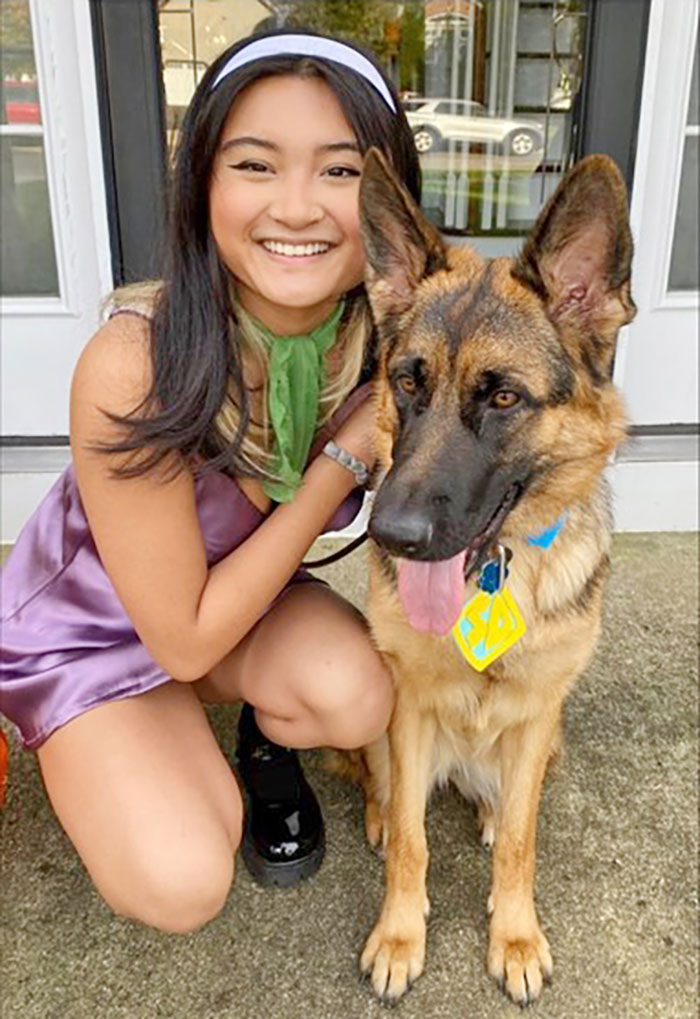 A picture of a girl dressed up as daphne from scooby doo and her dog in a scooby doo collar