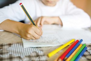 Child doing homework and writing story essay. Elementary or primary school class. Closeup of hands and colorful pencils.