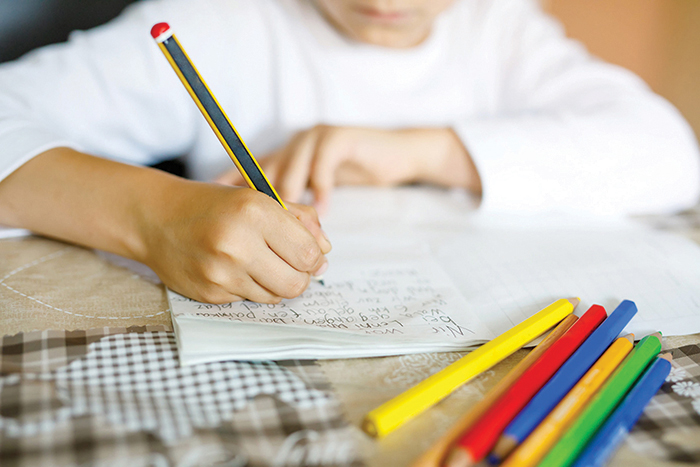Child doing homework and writing story essay. Elementary or primary school class. Closeup of hands and colorful pencils.