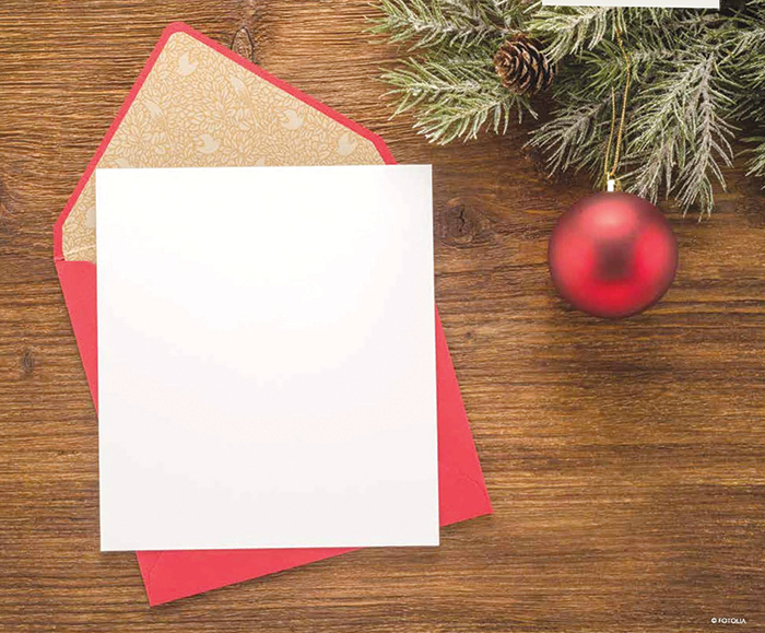 A blank christmas card, next to a wreath with an ornament hanging off of it