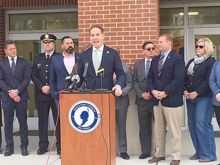 a group of individuals dressed in professional attire stand behind a man, speaking at a podium