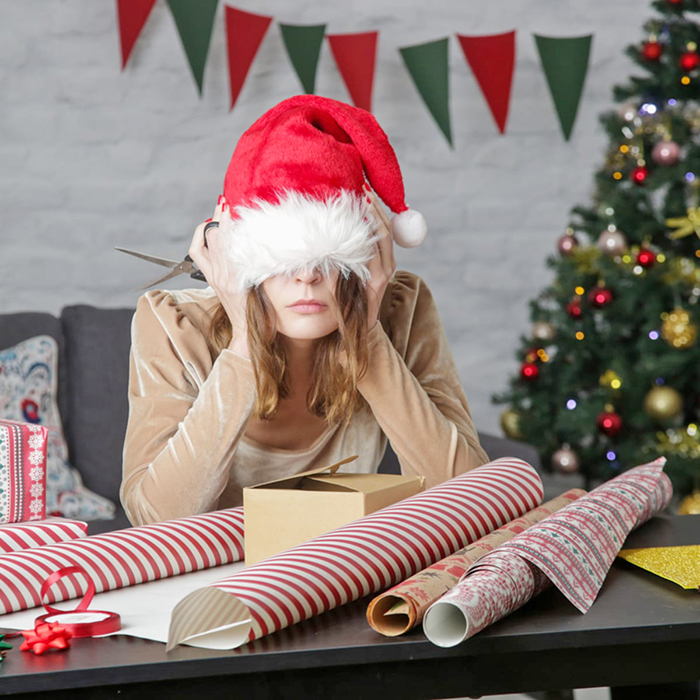 A lady with a santa hat on, looking disappointed in her wrapping abilities