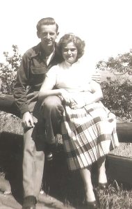 A black and white photo of a couple sitting on a fence, dressed up very nicely