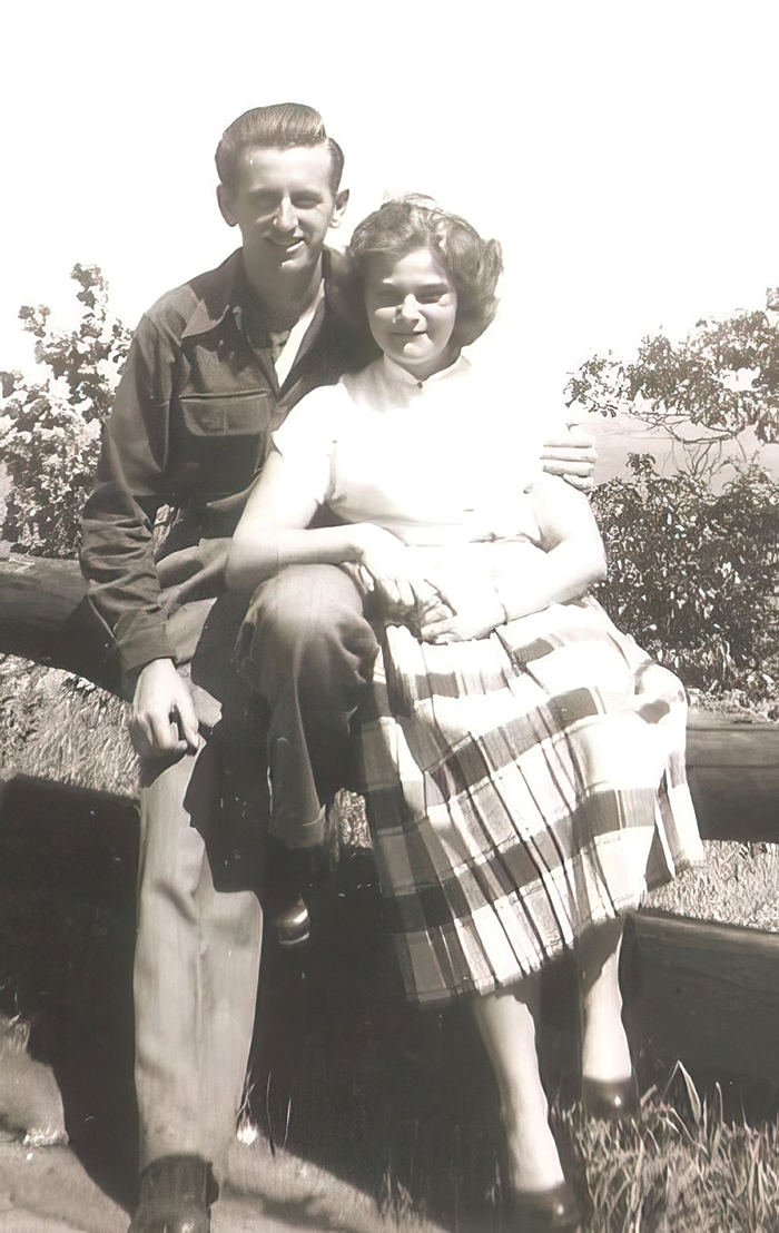 A black and white photo of a couple sitting on a fence, dressed up very nicely