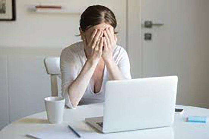 A picture of a lady holding her hands over her face in front of a computer.