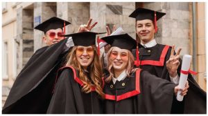A group of graduates, wearing black gowns with red striping, and their diplomas in hand.