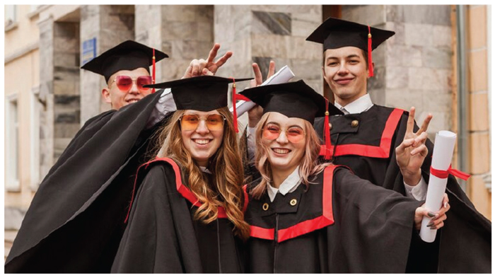 A group of graduates, wearing black gowns with red striping, and their diplomas in hand.