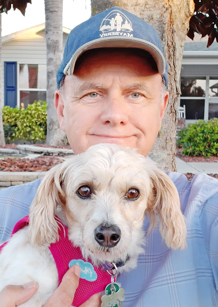 A man in a hat and button-down shirt with his dog, in a pink harness