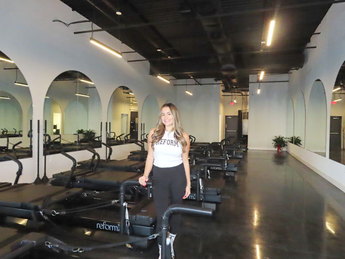A modern fitness studio featuring multiple reformer machines and large mirrors, enhancing the spacious and bright atmosphere.